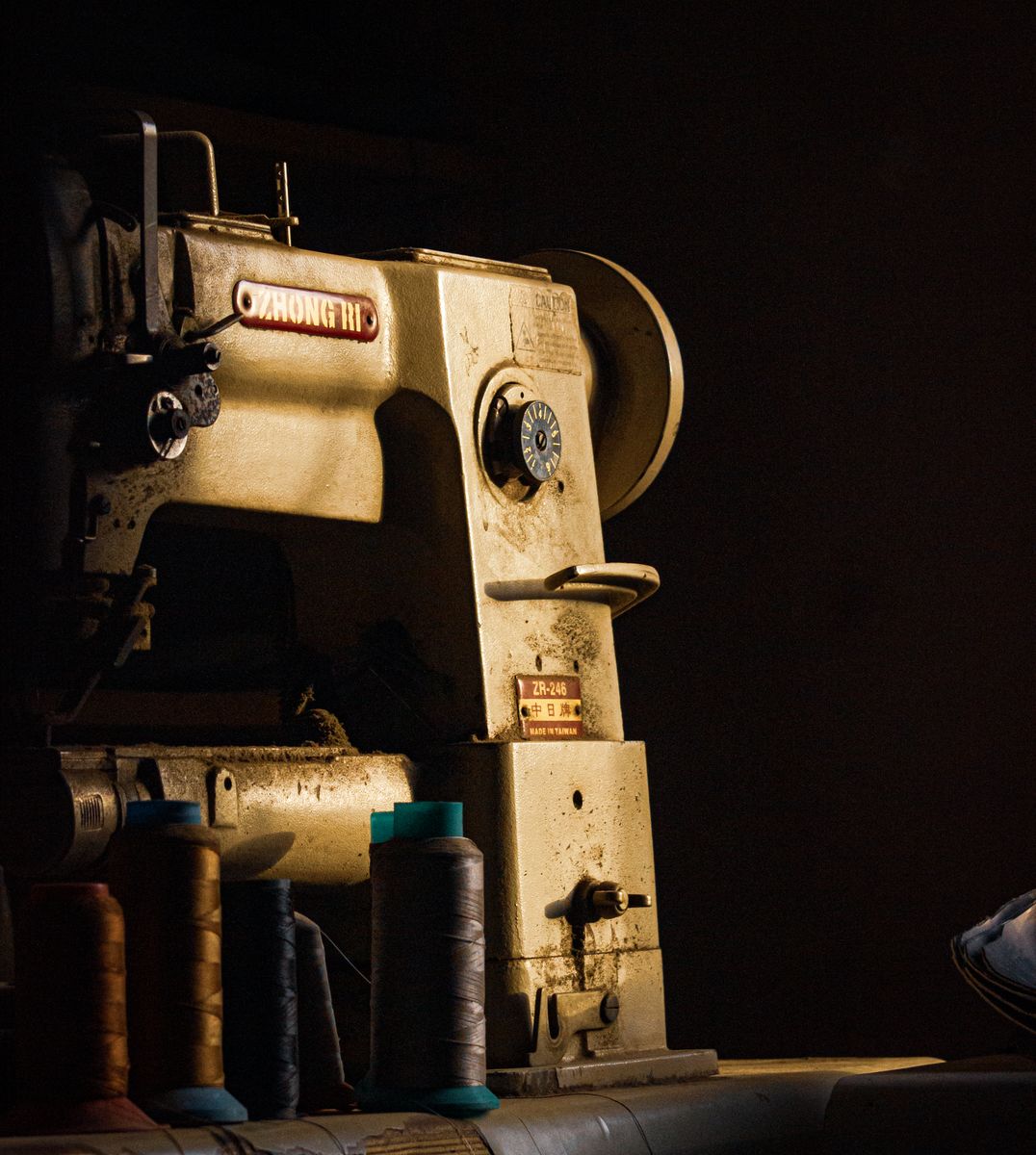 Classic industrial sewing machine and thread spools in warm, dramatic light
